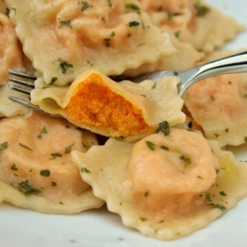 A closeup of a plate of carrot ravioli with one cut to show the filling