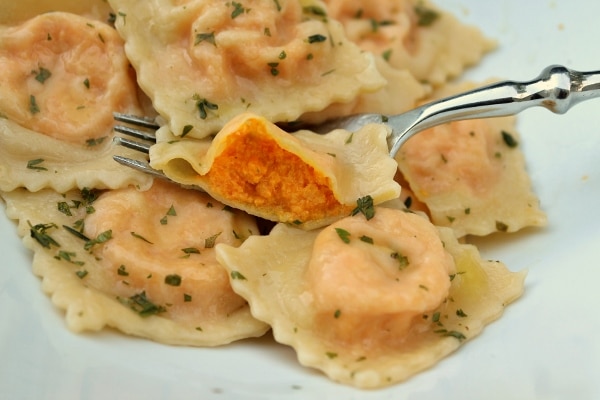 A closeup of a plate of carrot ravioli with one cut to show the filling