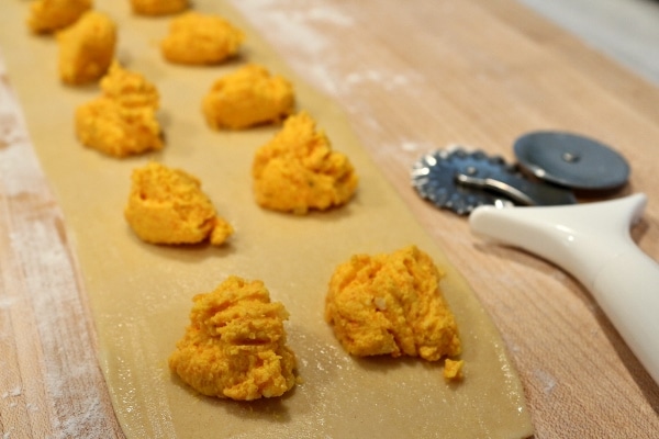 a strip of pasta dough on a wooden board topped with mounds of carrot filling