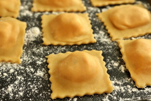 A closeup of homemade raviolis on a flour-dusted black surface