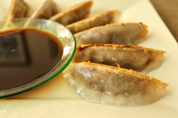 side view of pan-fried dumplings fanned out around a bowl of dipping sauce
