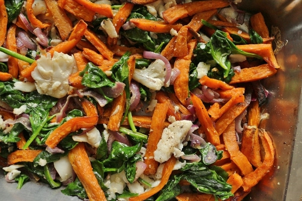 A pile of sweet potato fries mixed with cooked fish, spinach, and red onions