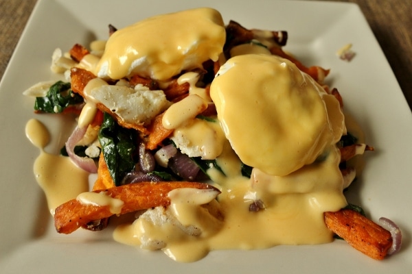 A plate of sweet potato fries and fish hash with eggs and Hollandaise sauce on top