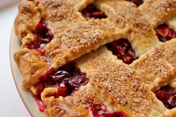 A closeup of a lattice topped cranberry pie with bubbly red filling peeking through