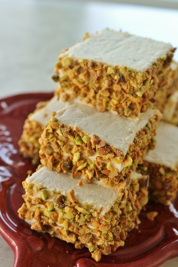 square marshmallows coated with chopped pistachios around the edges piled high on a small plate