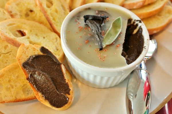 mushroom pate spread on a toasted baguette slice next to a white ramekin