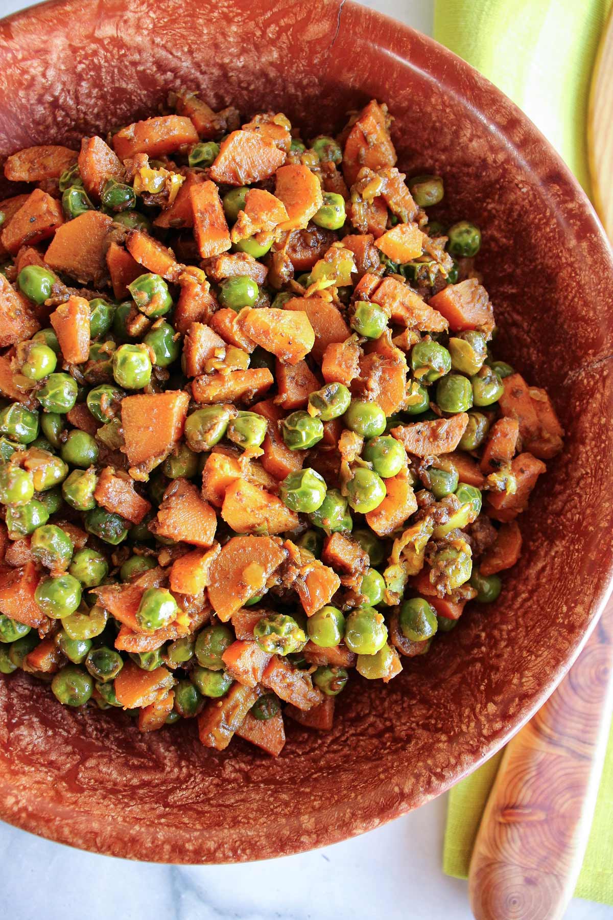 A rustic brown bowl filled with Indian gajar matar carrots and peas.