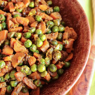 Closeup of Indian carrots and peas in a rustic brown bowl.