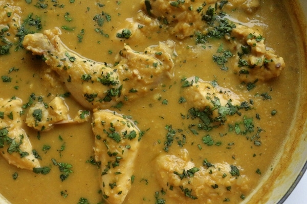 overhead view of chicken pieces cooked in a red lentil curry sauce in a pan