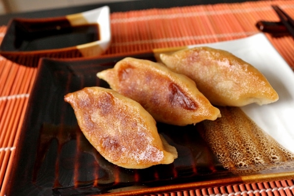 three pan-fried dumplings with their crispy bottoms facing up on a small plate