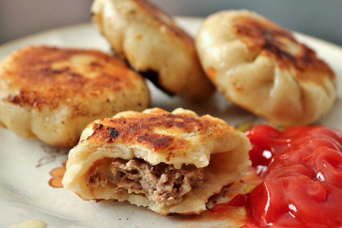 A closeup of a half-eaten cheeseburger dumpling on a plate with ketchup.