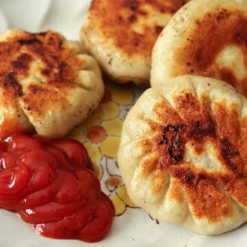 A plate of round pan-fried dumplings with ketchup on the side.