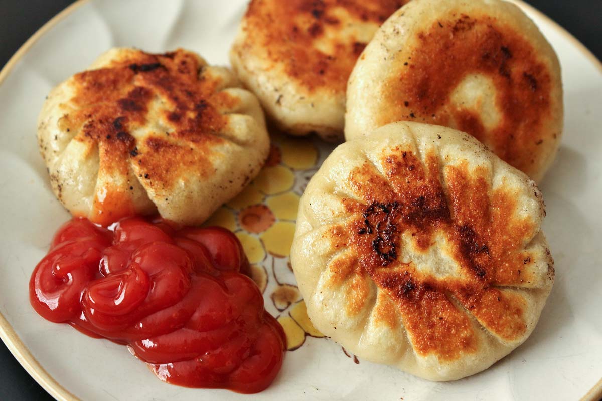 A plate of round pan-fried dumplings with ketchup on the side.