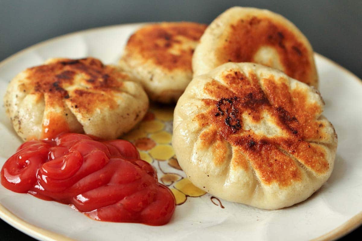 A closeup of round fried dumplings on a plate with a squirt of ketchup.