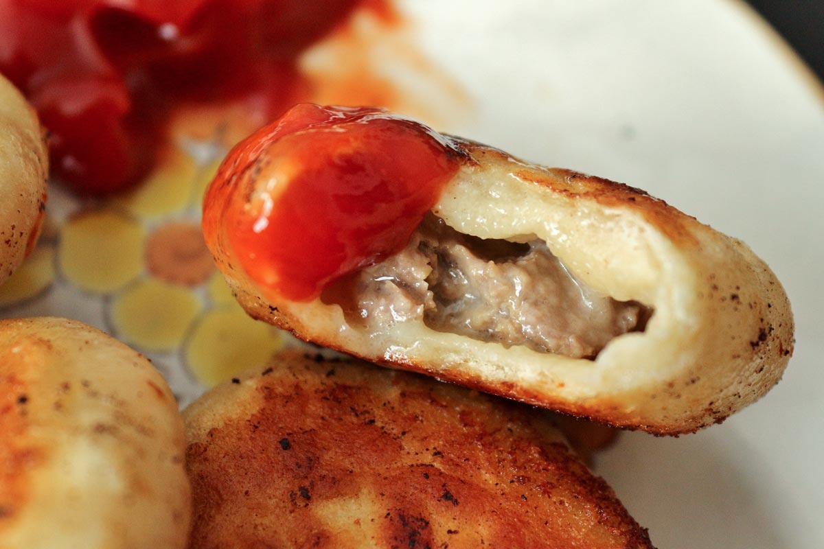 A closeup of a half-eaten cheeseburger dumpling dipped in ketchup.