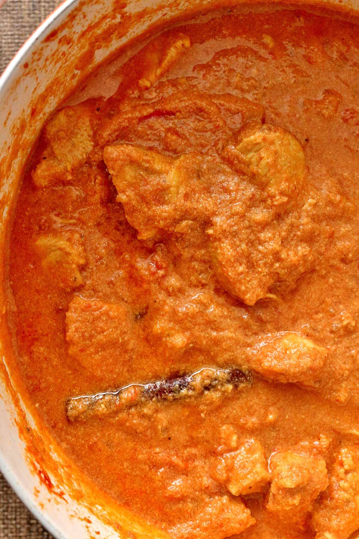 A pot of creamy Indian chicken curry with a visible cinnamon stick.