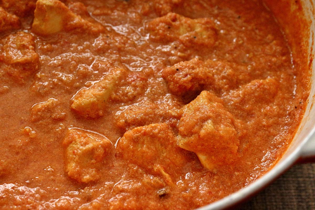 Closeup of chicken pieces in a creamy tomato curry sauce.