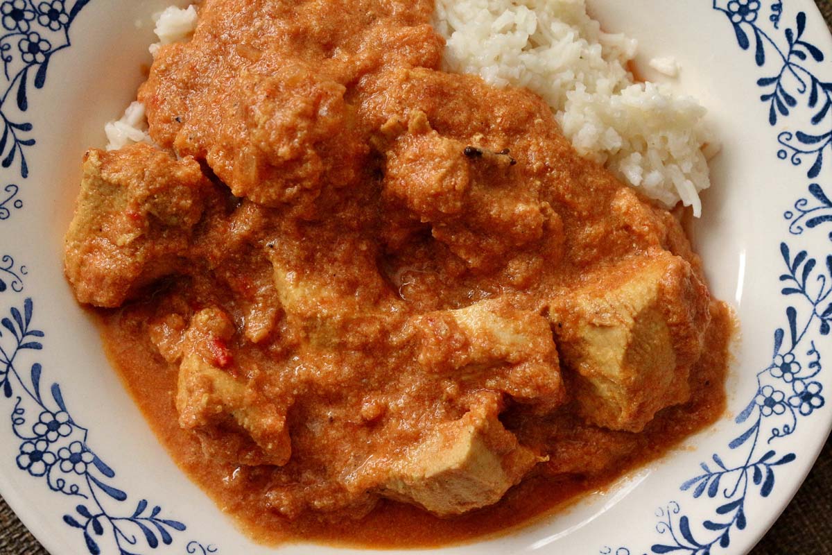 Chicken curry in creamy tomato sauce served with white rice in a shallow bowl.