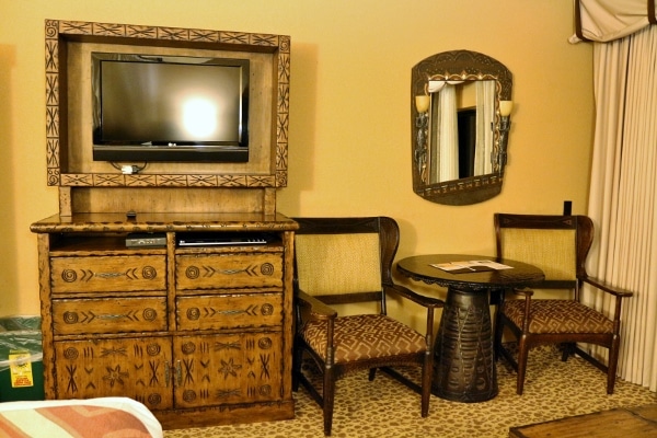 a television, dresser, table and chairs inside a hotel room