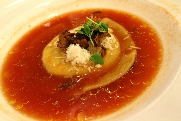 a large ravioli in a bowl of tomato broth
