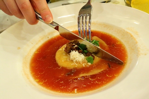 a knife and fork cutting a large ravioli in half