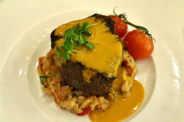a filet mignon steak served over tomato risotto with an orange-colored sauce