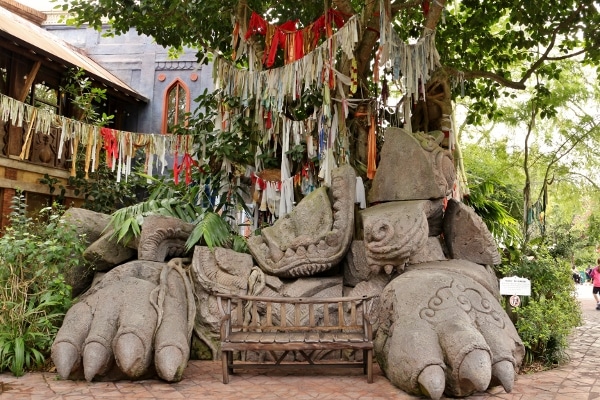 a stone sculpture, bench, and hanging fabrics beneath a tree