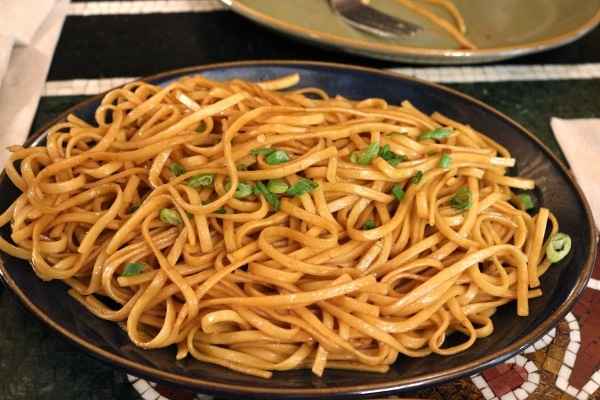 a plate of garlic noodles garnished with chopped scallions