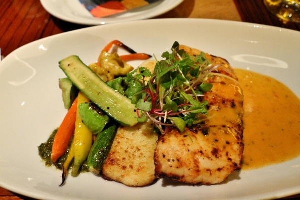 A plate of fish served with vegetables and microgreens on top