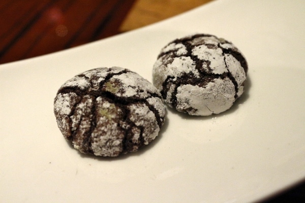 two crackly chocolate cookies with powdered sugar on a white plate