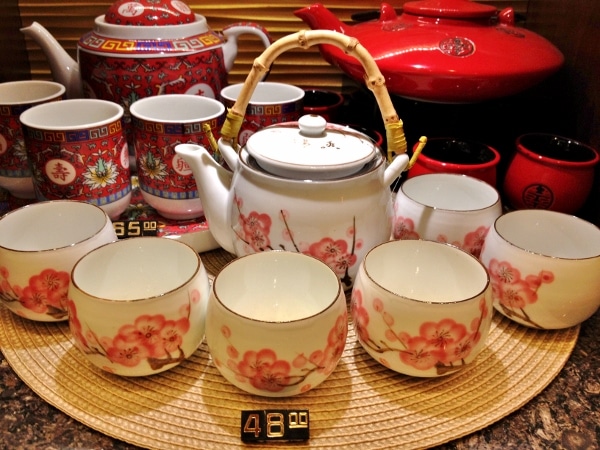 a small white teapot with teacups painted with images of pink cherry blossoms