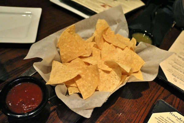 a basket of tortilla chips with cups of red and green salsa