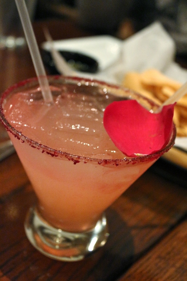 a pink-colored margarita in a glass with a rose petal garnish