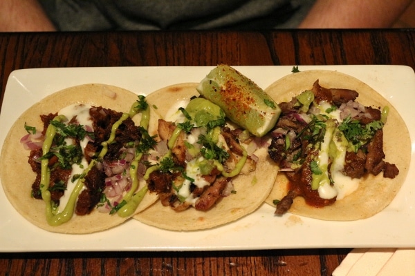 A plate of three meat tacos with guacamole sauce and a lime wedge