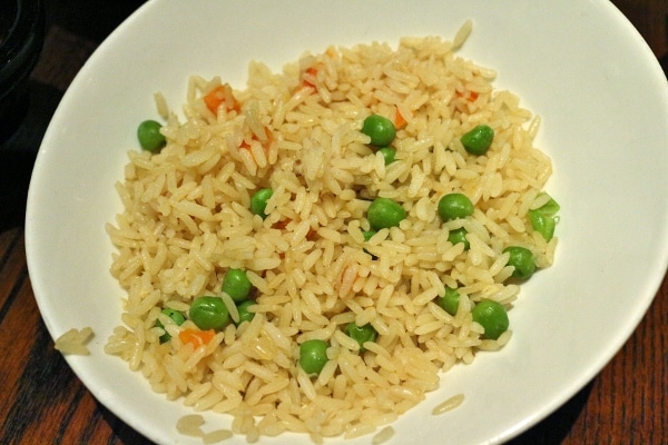 A bowl of rice with carrots and green peas
