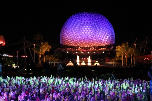 A view of Spaceship Earth lit up at night with colorful flowers in front