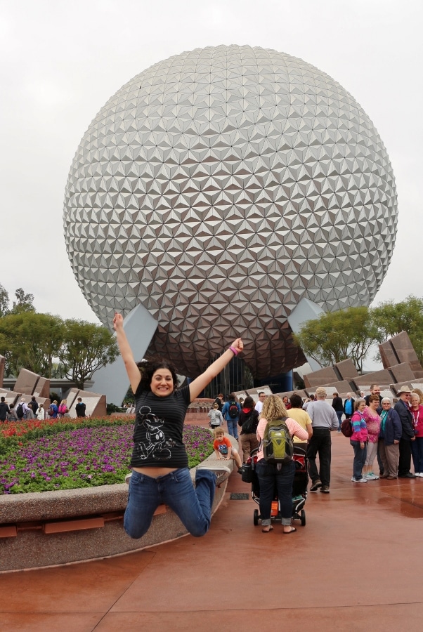 A woman jumping in front of Spaceship Earth in Disney\'s Epcot park