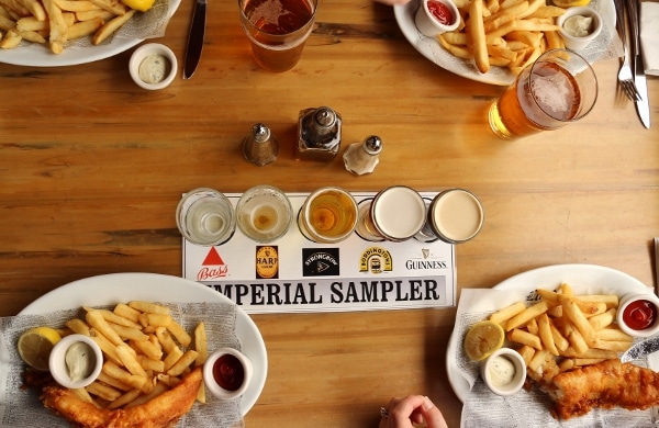 overhead view of a wood table with plates of fish and chips and a beer flight