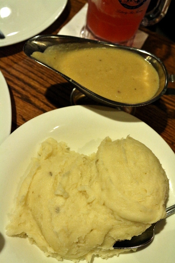 A plate mashed potatoes with a gravy boat of gravy to the side