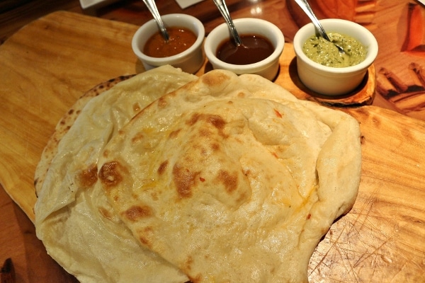 a platter of naan with three dipping sauces on the side