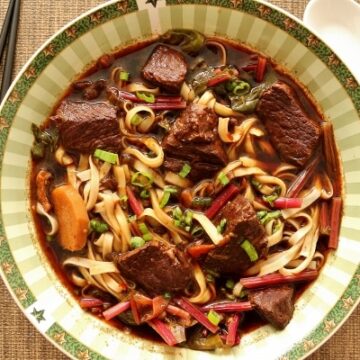 overhead view of a bowl of beef noodle soup with chopsticks on the side