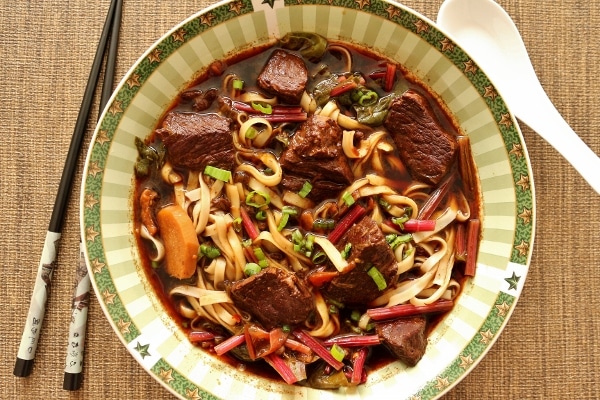 overhead view of a bowl of beef noodle soup with chopsticks on the side