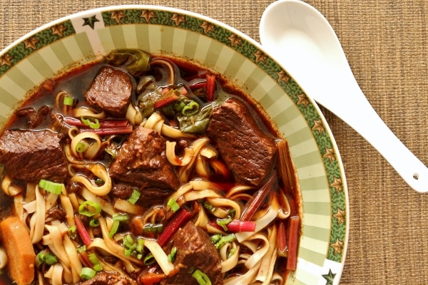 overhead closeup of a bowl of beef noodles soup with an Asian style spoon on the side