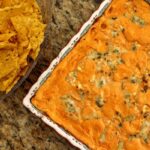 overhead view of a square baking dish of buffalo chicken dip with chips on the side