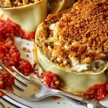 a closeup of an eggplant rotolo topped with bread crumbs on a plate with a fork