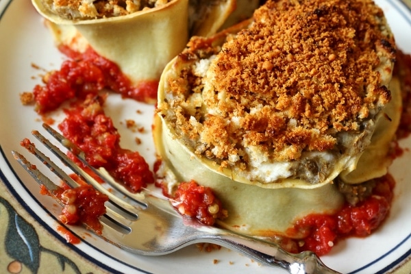 a closeup of an eggplant rotolo topped with bread crumbs on a plate with a fork