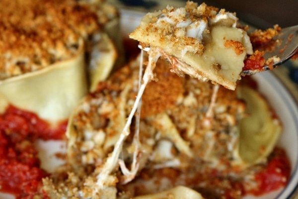 A closeup of a forkful of pasta lifting up from a plate with strings of cheese