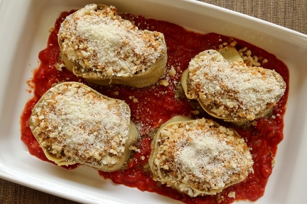 overhead view of pasta roll ups topped with bread crumbs and cheese in a baking dish