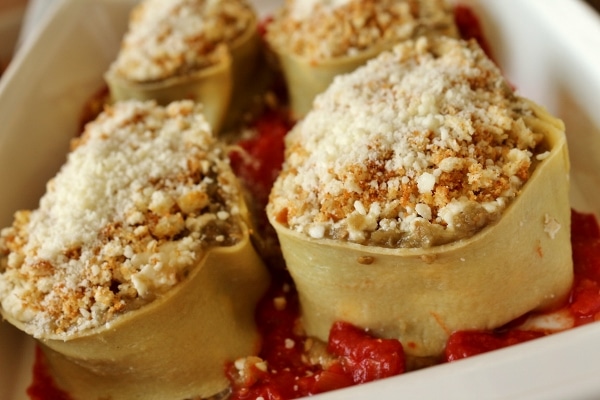 A closeup side view of a baking dish of unbaked eggplant and parmesan rotolo