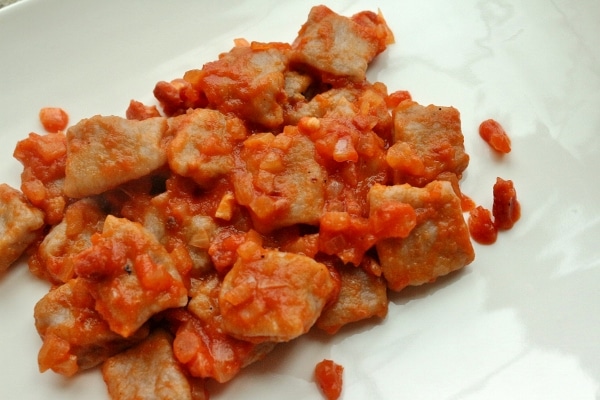 a white plate topped with gnocchi in tomato and pancetta sauce